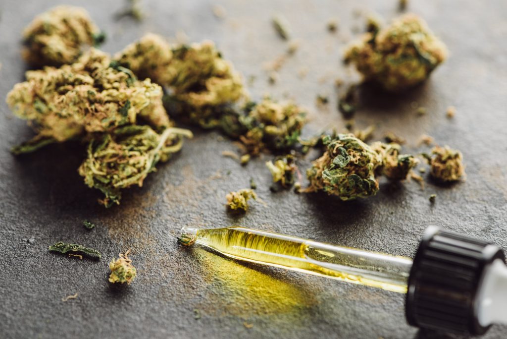close up view of medical marijuana buds and dropper with hemp oil oil on marble surface